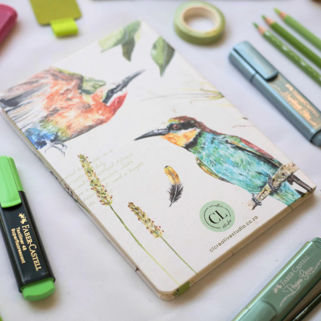 African Bird Journal with Bee Eater design surrounded by stationery items on a white surface