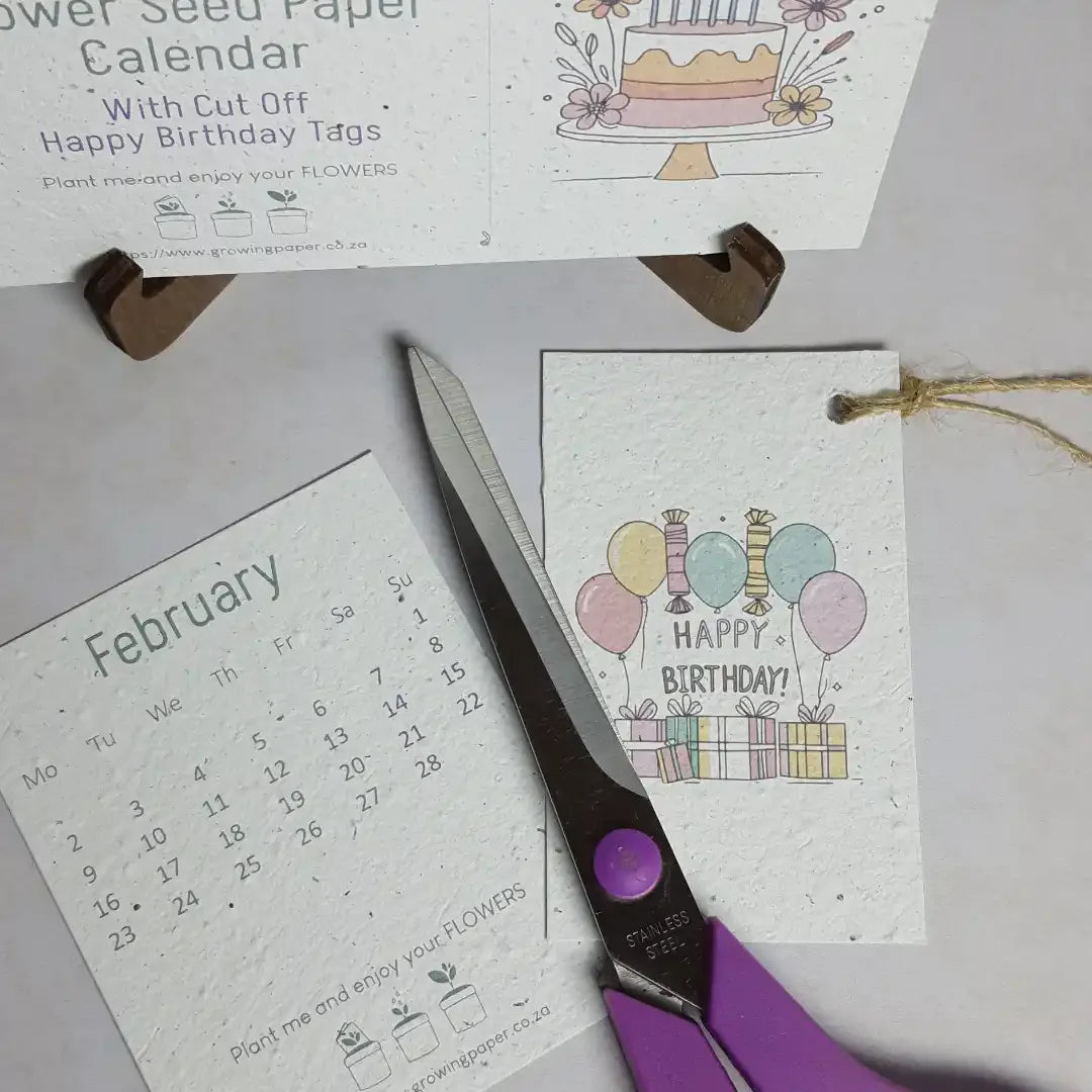 Calendar with cut-off birthday tags, scissors, and a seed paper card on a light surface.