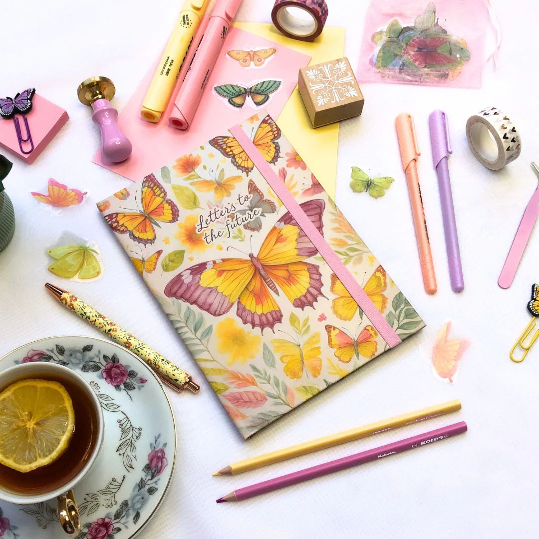 Letters to the future Journal with butterfly design surrounded by stationery items on a white surface