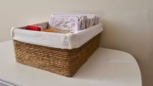 100% Natural Jute basket with a white liner on a surface, containing items including a red object and a box of tissues.