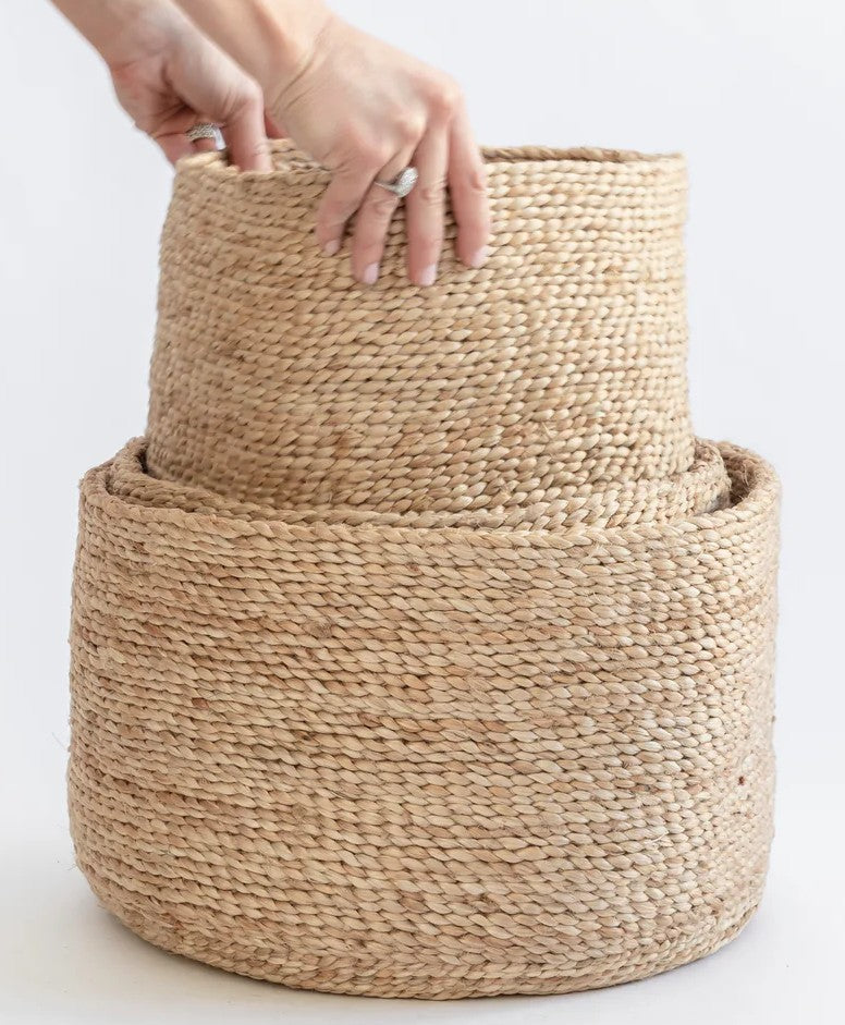 Stack of Natural eco-friendly Jute baskets with a hand reaching to touch the top one on a light background