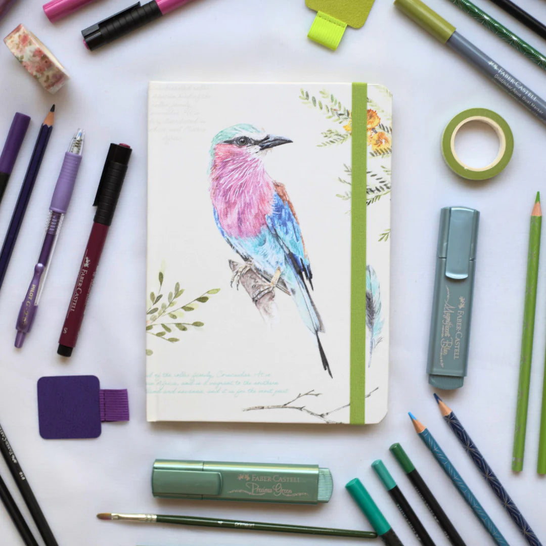 African Bird Journal with Lilac Breasted Roller design illustration surrounded by stationery items on a white background