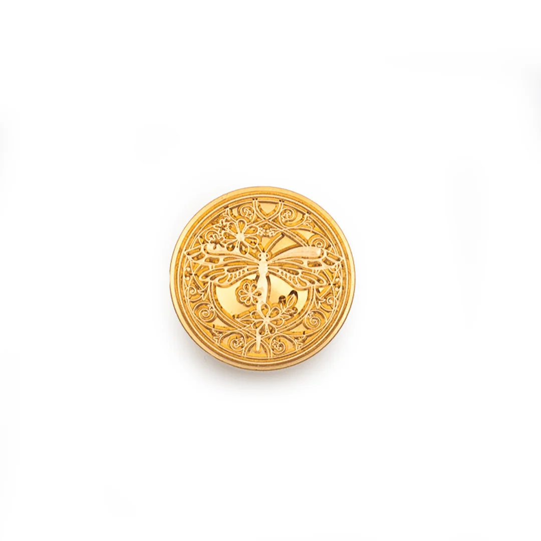 A round gold stamp-seal featuring an intricate filigree dragonfly design, centered on a plain white background.