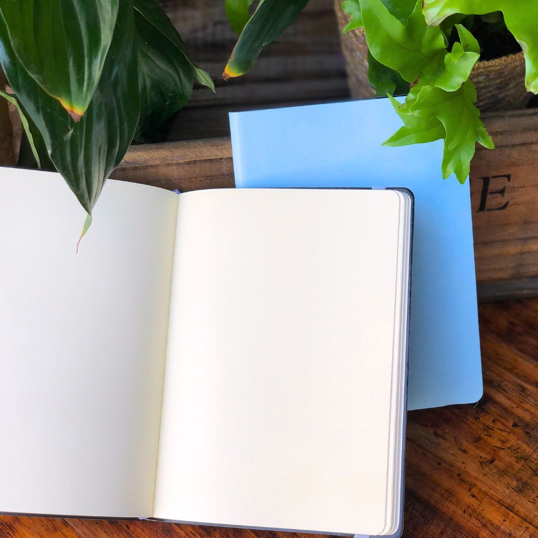 Open Insect Hardcover Journal showing blank pages on a wooden surface with plants in the background