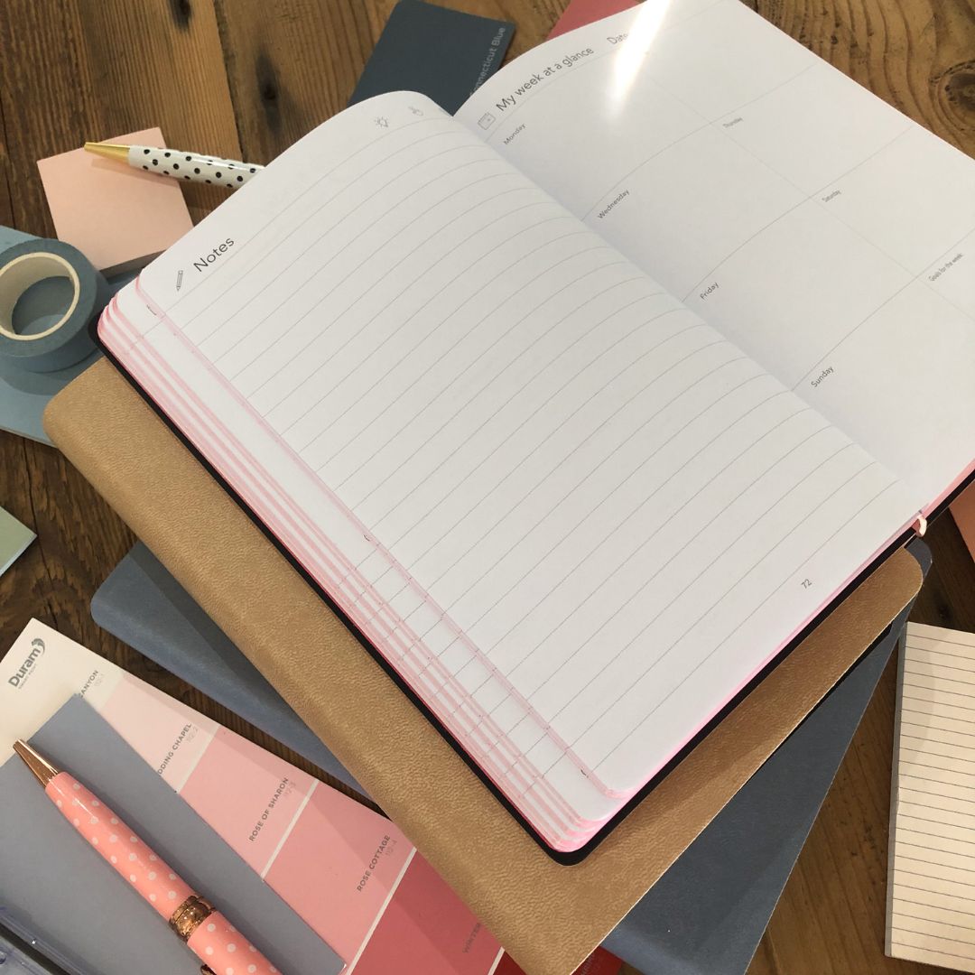 Open multi planner with inside pages on a wooden surface with stationery items.