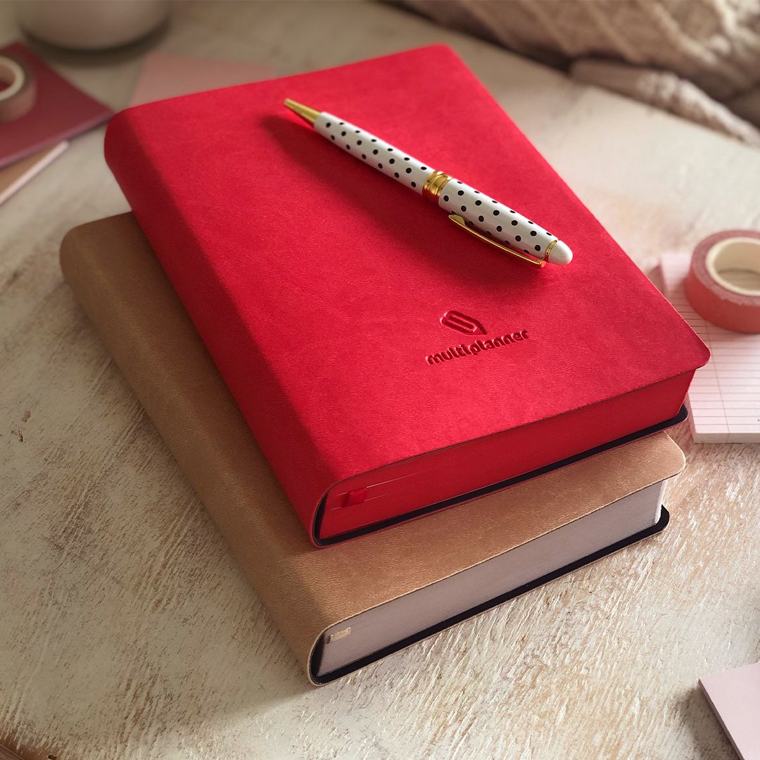 Red multi planner placed on a wooden surface and a dotted pen on top of the multi planner