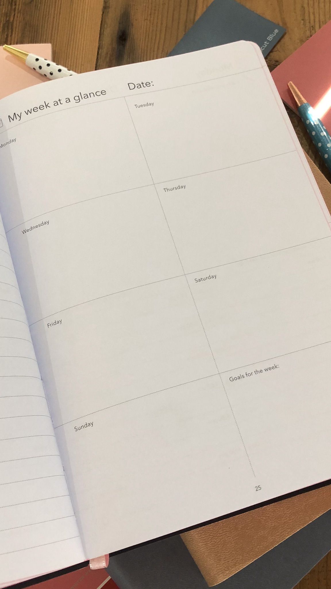 Weekly planner with week at a glance inside pages with dotted pens and small notebook on a wooden surface
