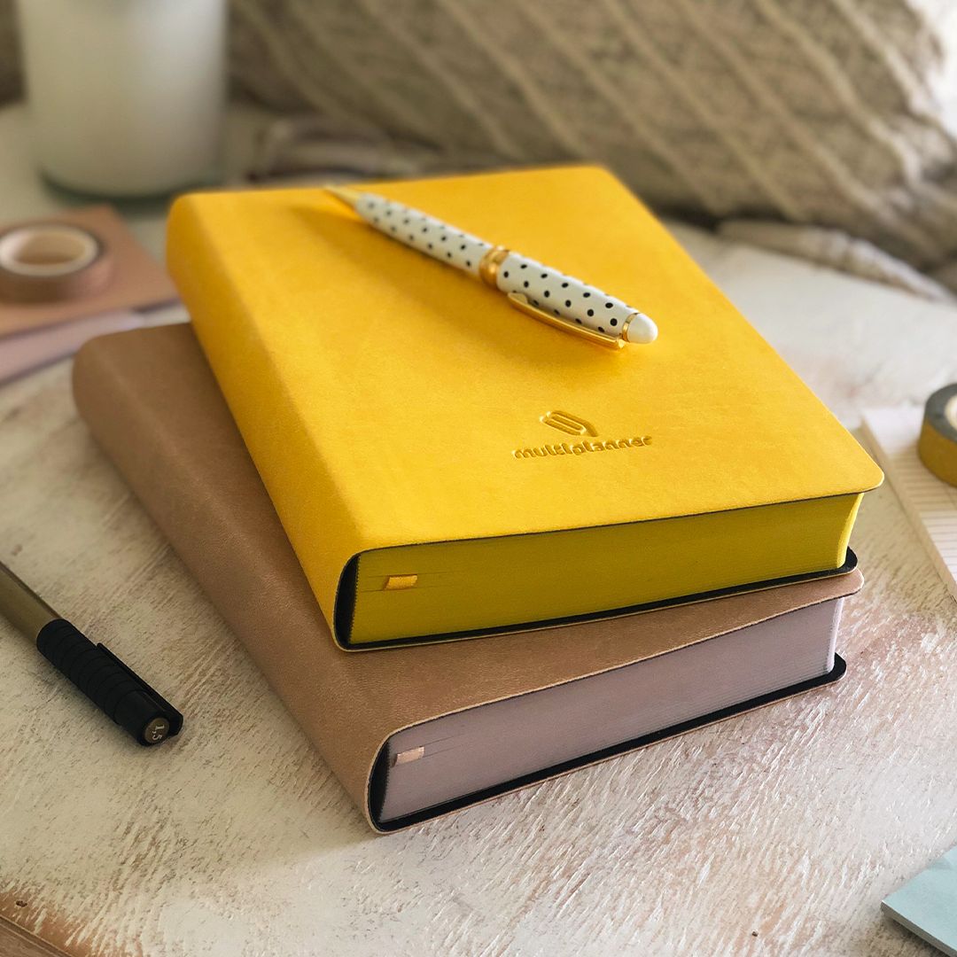 Yellow and tan multi planners with a dotted pen on a wooden surface