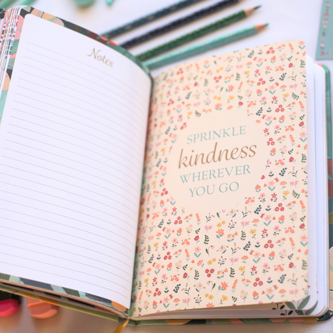 Journal with floral design on inside pages with 'Sprinkle kindness wherever you go' text, surrounded by colorful pencils.