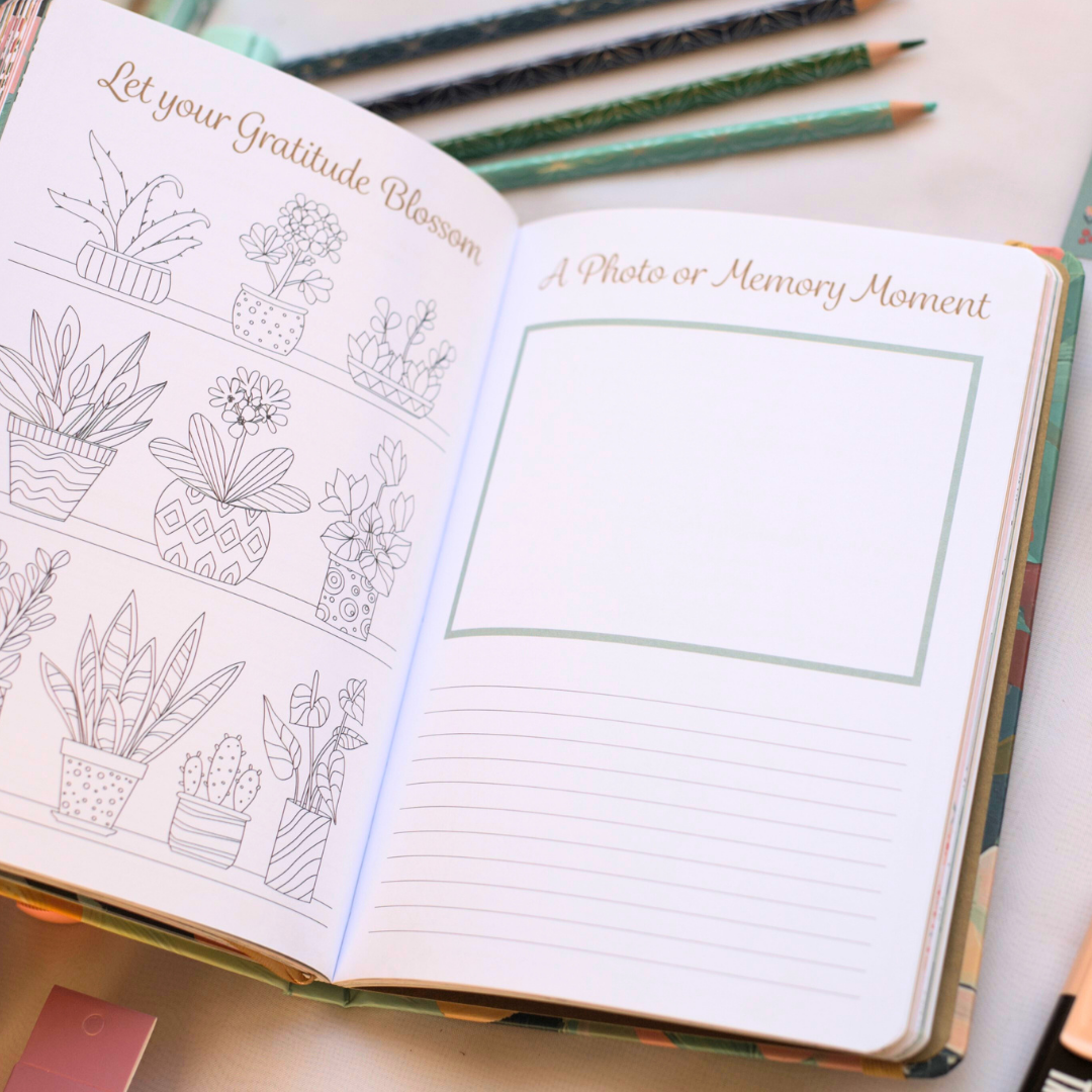 Open journal with plant illustrations and blank page and lines, surrounded by pencils.