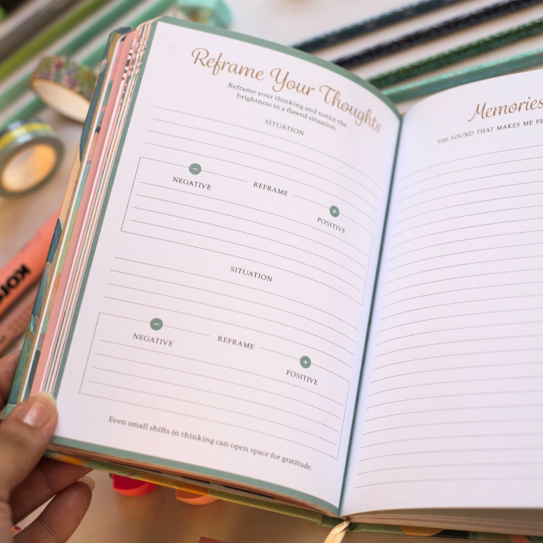 Open journal with a page titled 'Reframe Your Thoughts' held by a hand to develop the mind