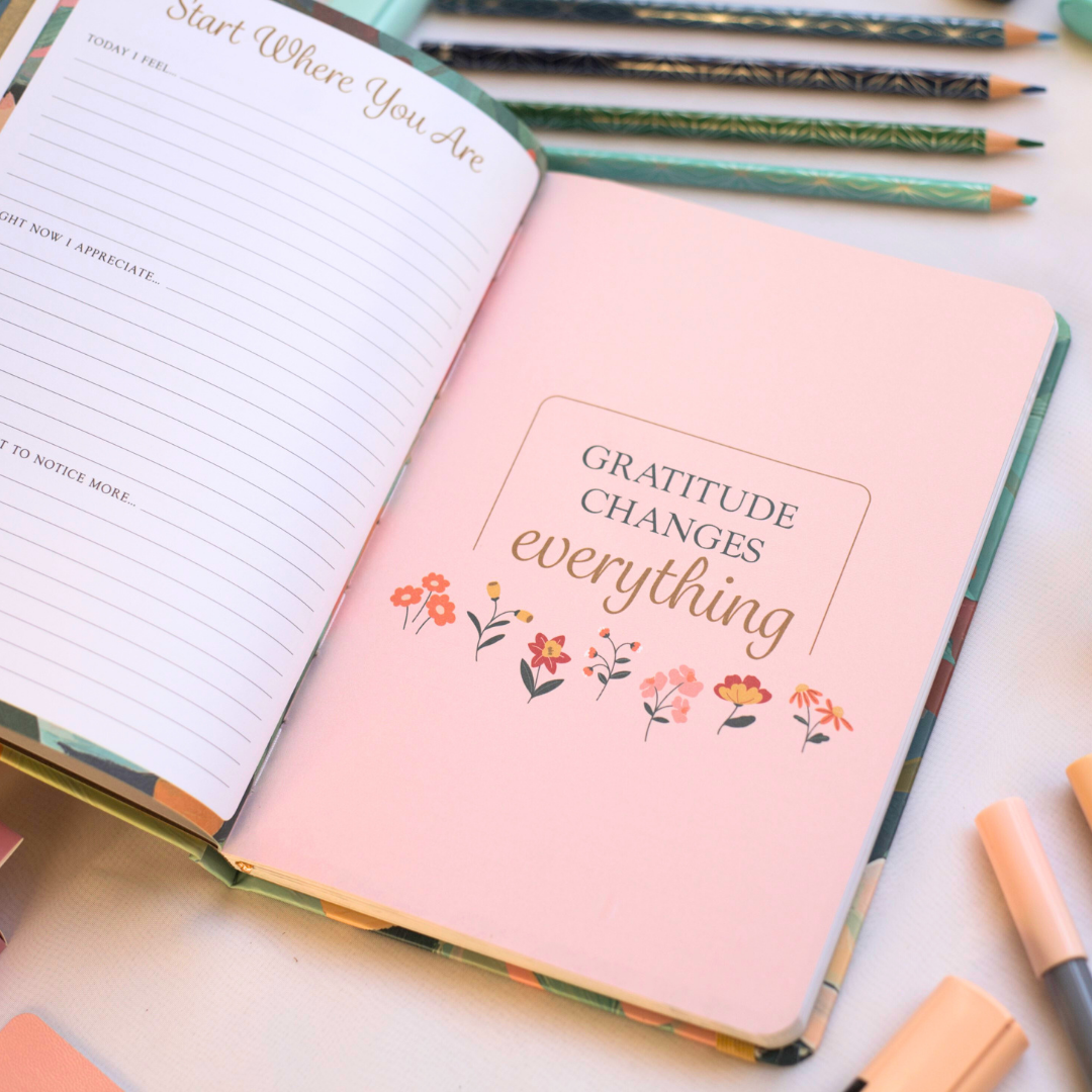 Inside pages of journal with 'Gratitude Changes Everything' quote, surrounded by stationery items on a light surface.
