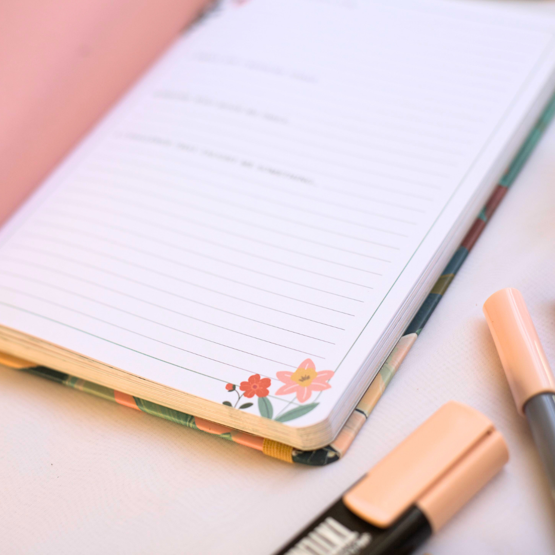 Inside pages of Journal with floral design on the cover, accompanied by a pen and highlighter on a light background