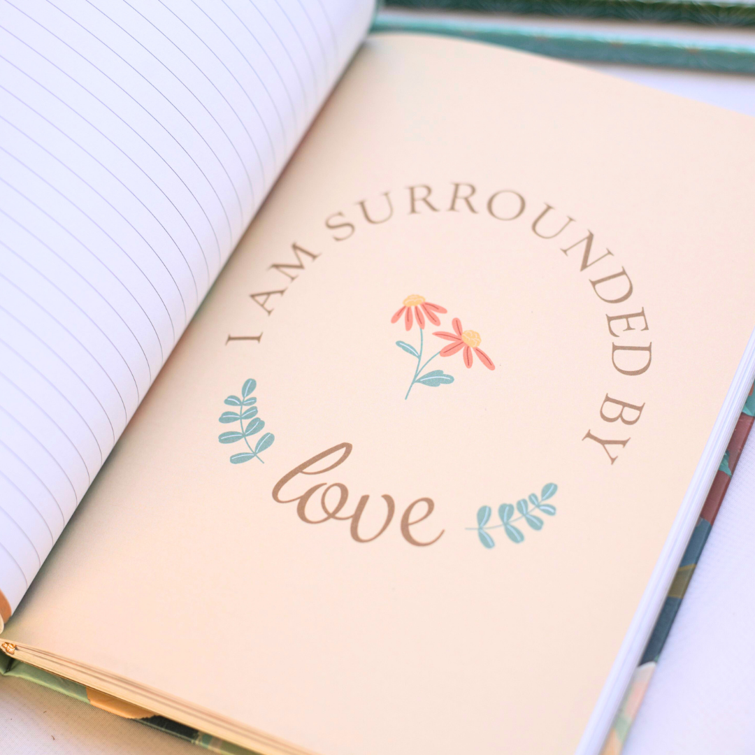 Open journal with 'I am surrounded by love' text and floral designs on a white background