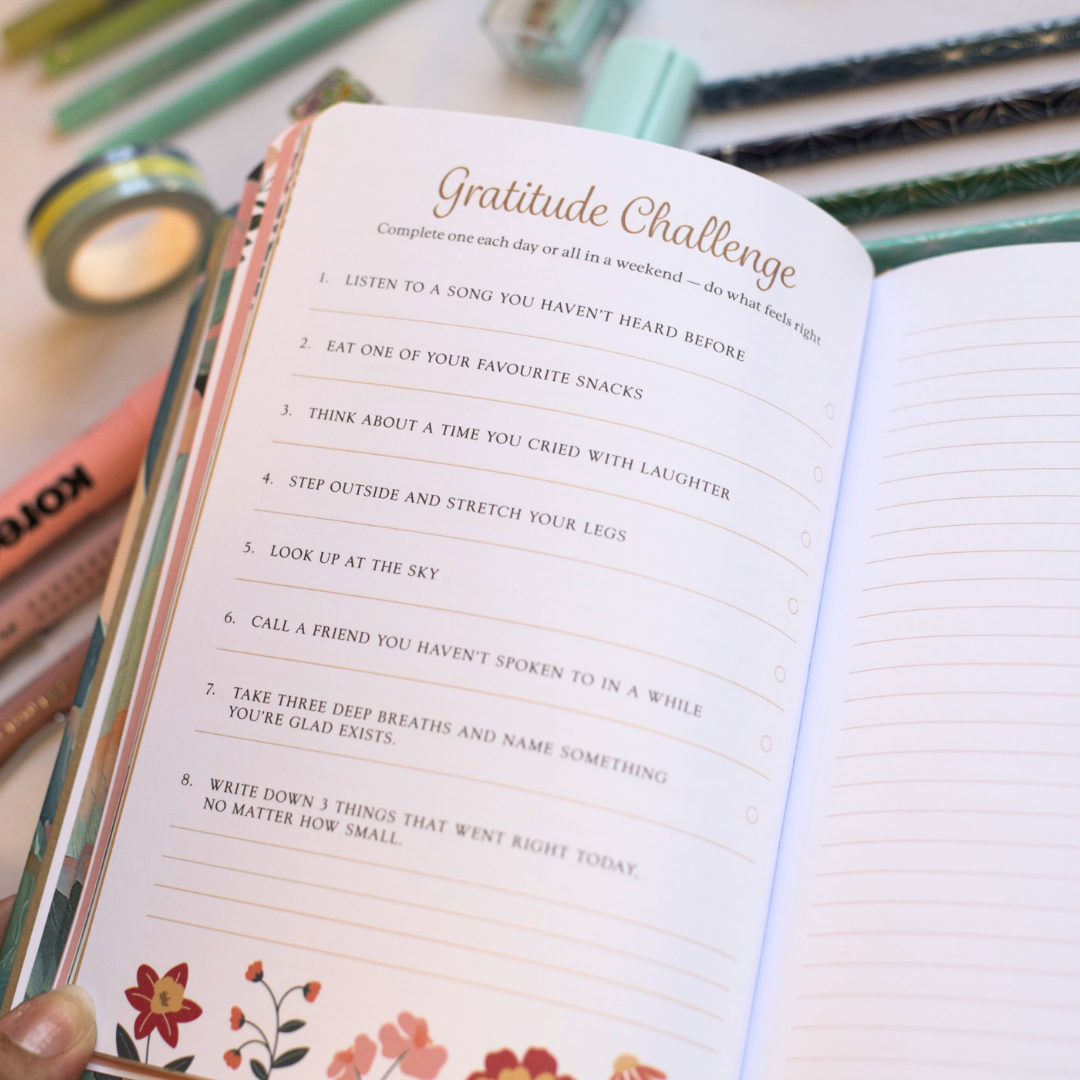 Interactive page inside journal titled 'Gratitude Challenge' with stationery items on a surface