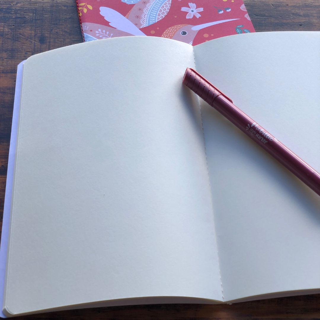Open pink notebook with blank pages and a pink pen on a wooden surface