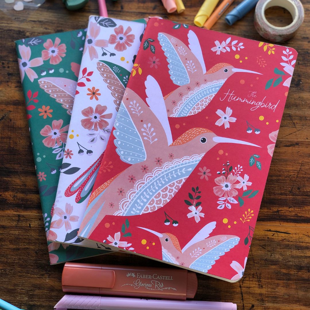 Three colorful notebooks set with bird and floral designs on a wooden surface.