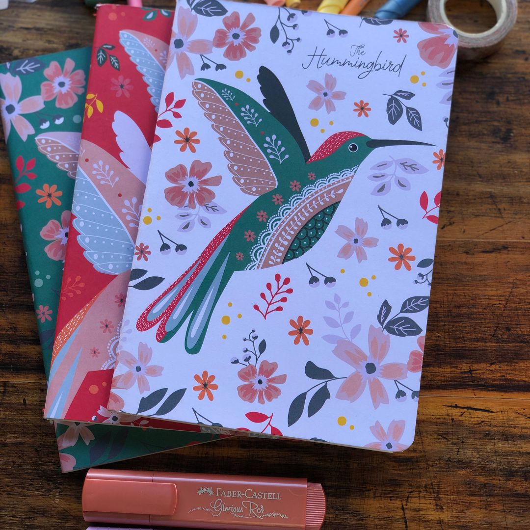 Set of 3 Hummingbird Notebooks A5 with a colorful hummingbird designs on a wooden surface, with a Faber-Castell product in the foreground.