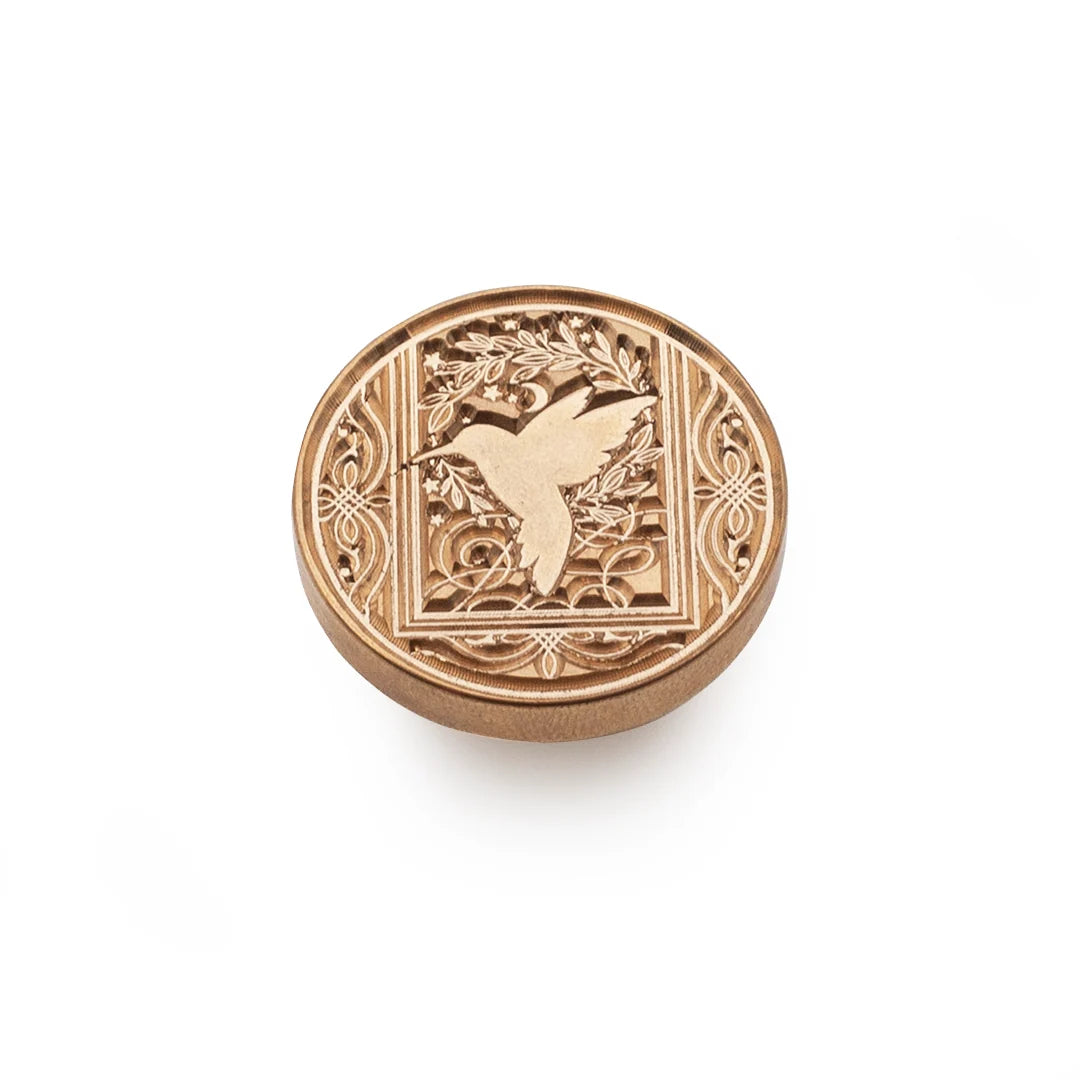 A round, bronze-toned metal stamp-seal with an embossed hummingbird and floral scrollwork design, shown on a clean white background.