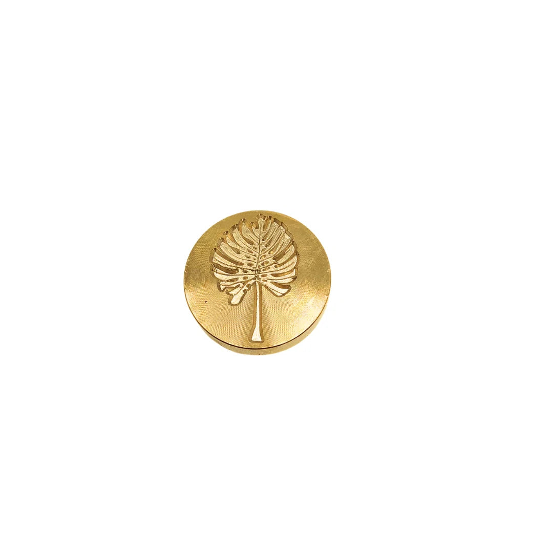 A single round gold-toned stamp-seal with an embossed palm tree design, centered on a plain white background.