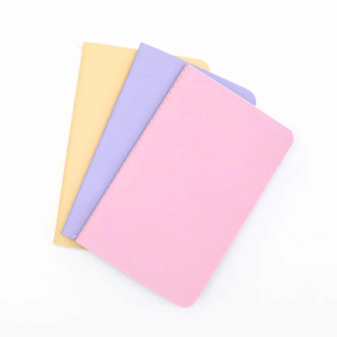 Three colorful pastel 'Love and Macaron' notebooks in pink, purple, and yellow on a white background