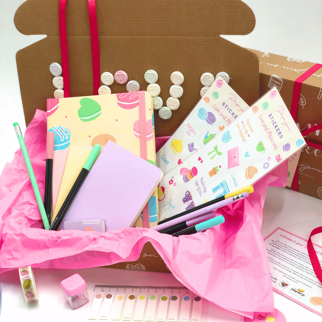 Love and Macaron Gift Box with Stationery pastel themed items including notebooks, pens, and stickers in a decorative box with pink ribbon.