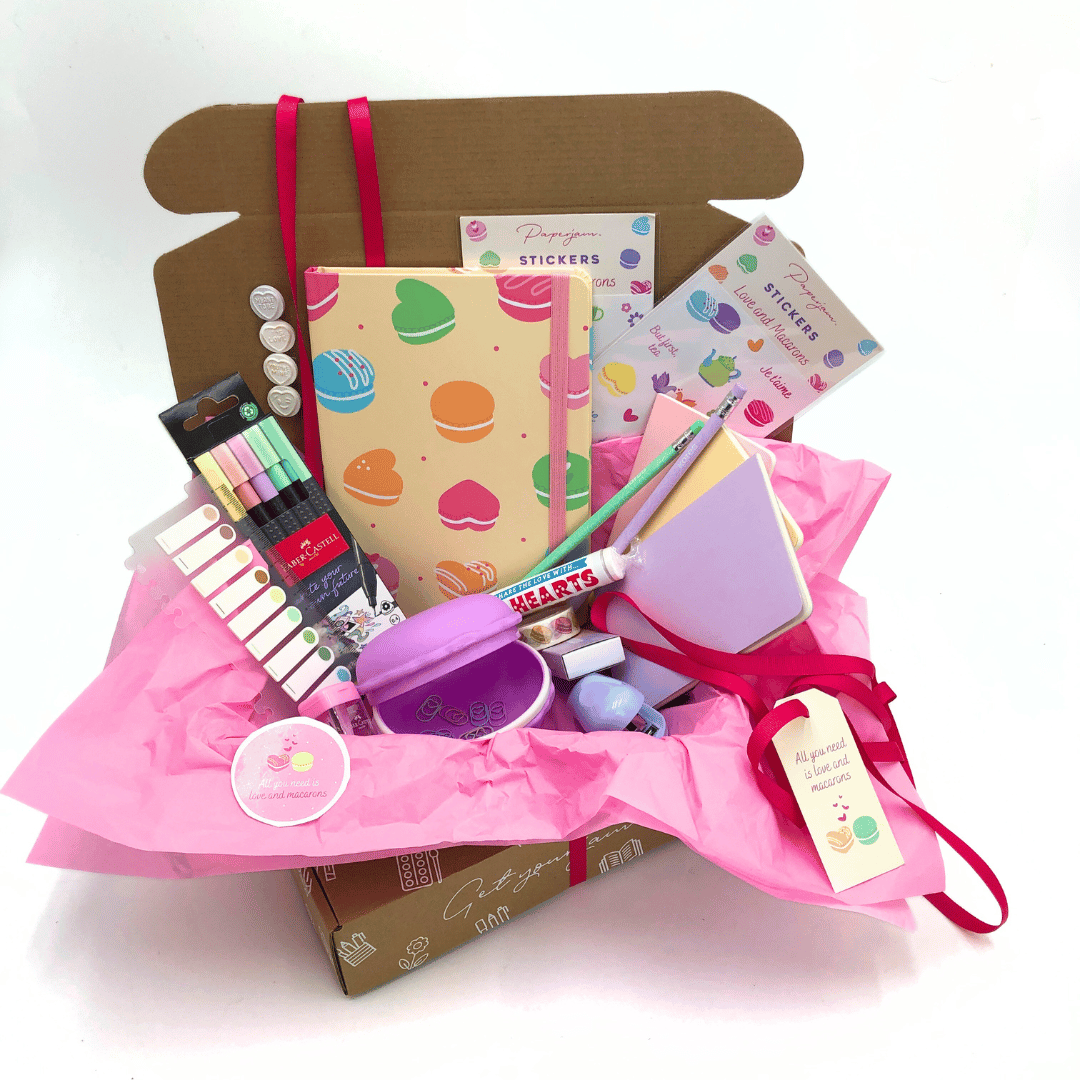 Love and Macaron Gift Box has stationery items including a notebook, stickers, and other stationery goodies in pink pastel on a white background