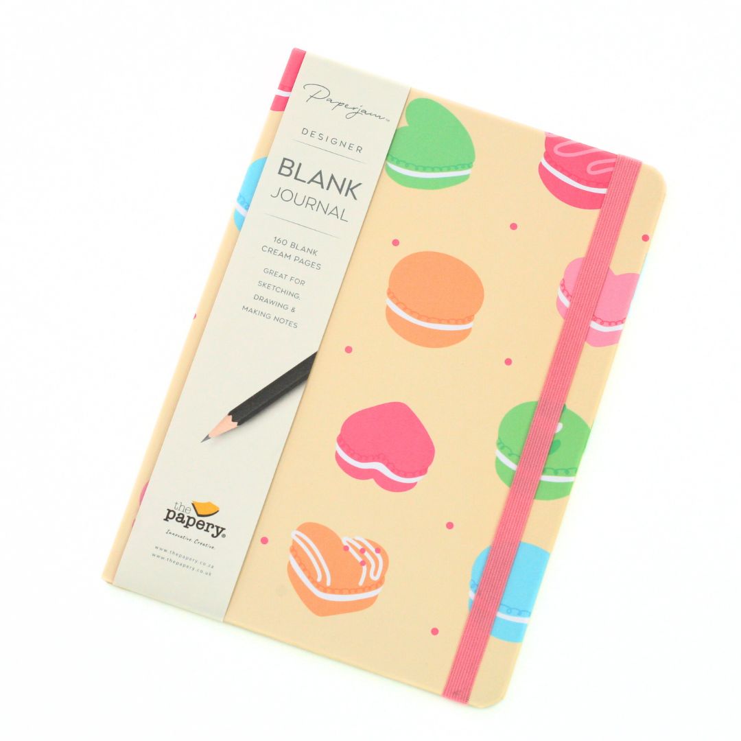 A Pappygoose Designer Blank Journal with a pastel macaron pattern on a cream cover, shown with its paper sleeve and included pencil on a white background.