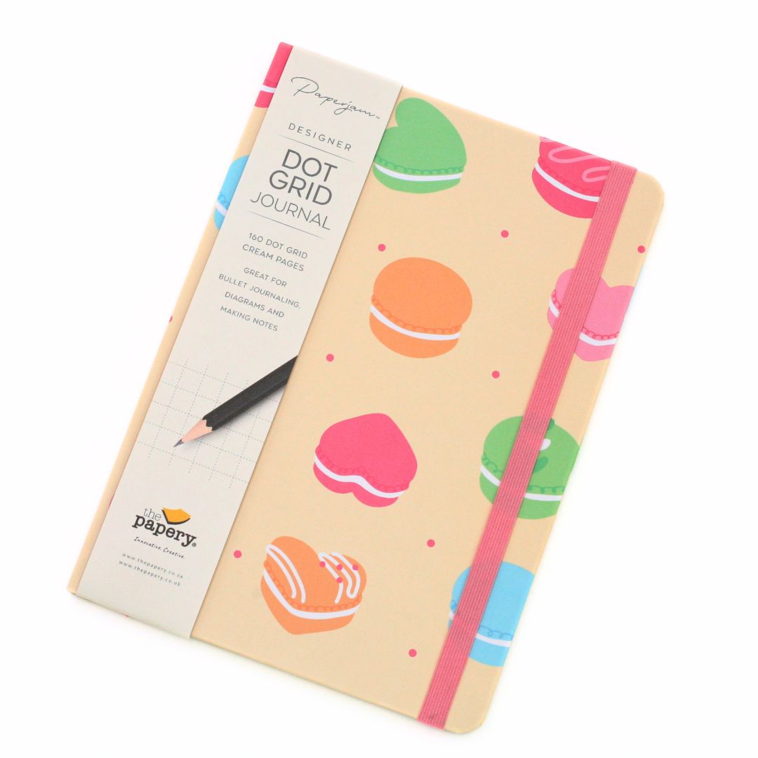 A Papergame Designs Dot Grid Journal with a cream-colored cover decorated with colorful macaroni illustrations and a pink elastic closure band. The journal is shown with its paper sleeve on a clean white background.