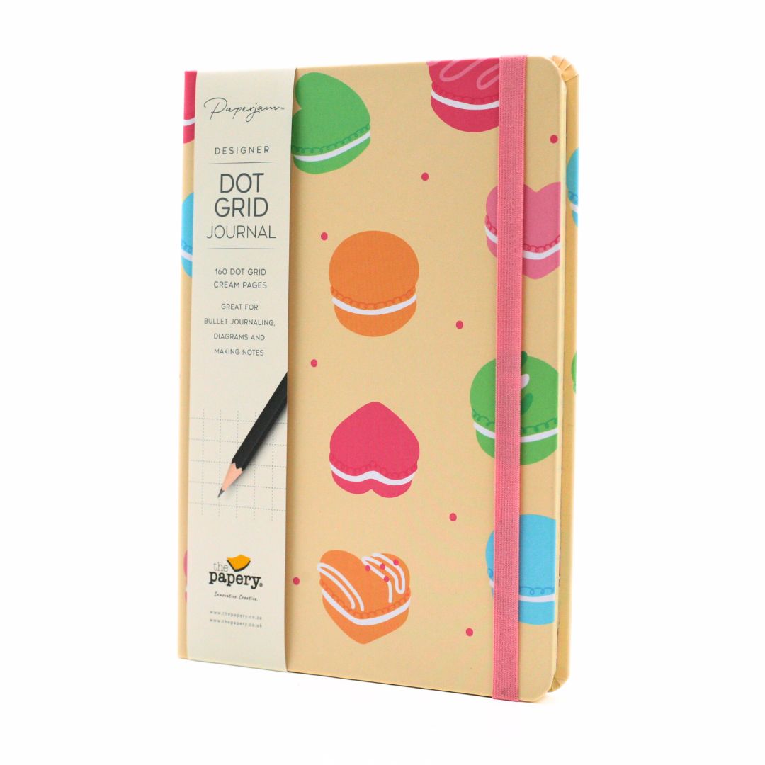 Papery Designers Dot Grid Journal with a cream-colored cover decorated with colorful macaron illustrations, featuring a pink elastic closure band and a black pencil on the side.