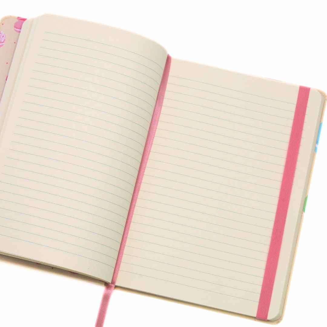 An open lined notebook with cream-colored pages, a pink elastic closure, and a pink ribbon bookmark, shown on a white background.