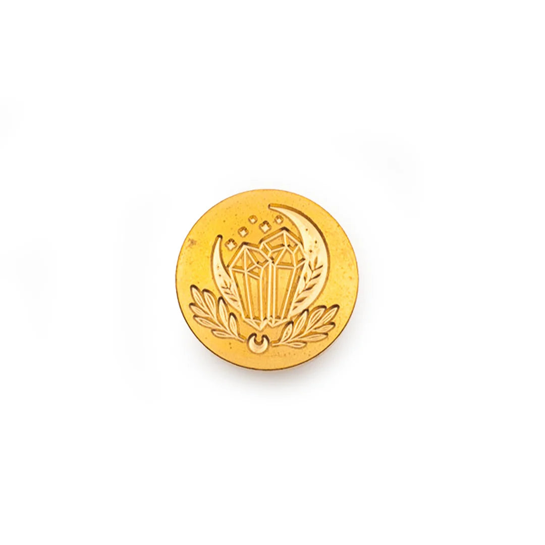 A round gold-colored metal stamp-seal featuring an embossed crescent moon, diamond, and laurel wreath design, centered on a plain white background.