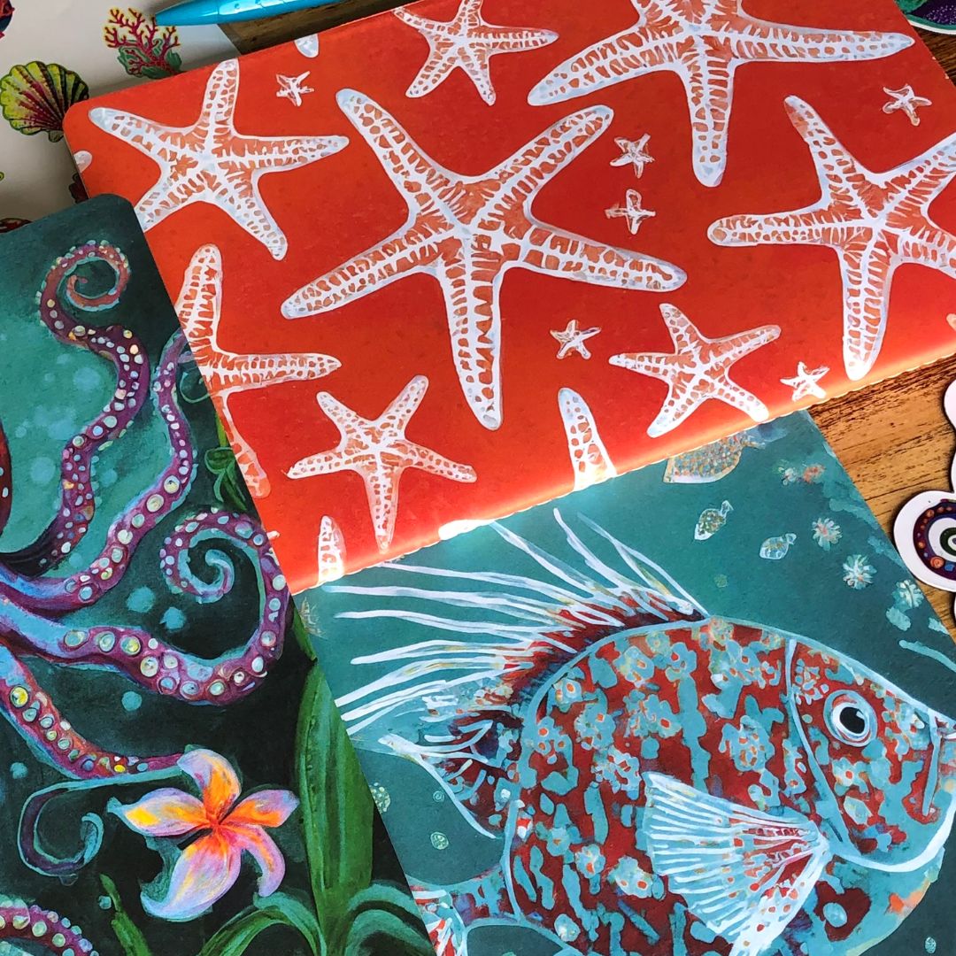 Colorful Ocean Treasures Notebooks A5 with ocean-themed designs including starfish, octopus, and fish on a wooden surface.