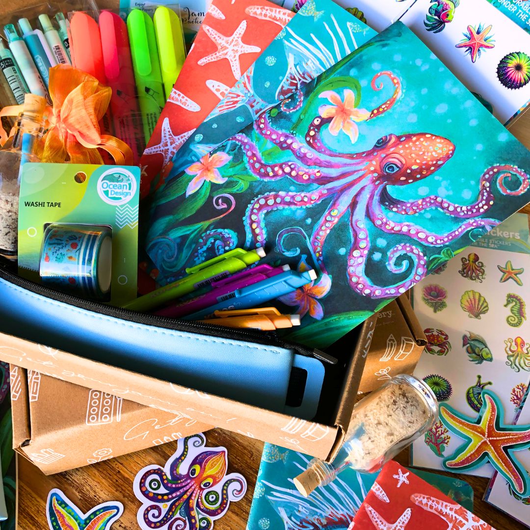 Ocean Treasures Gift box has colorful stationery items including a notebook with an octopus design, markers, and stickers on a wooden surface.