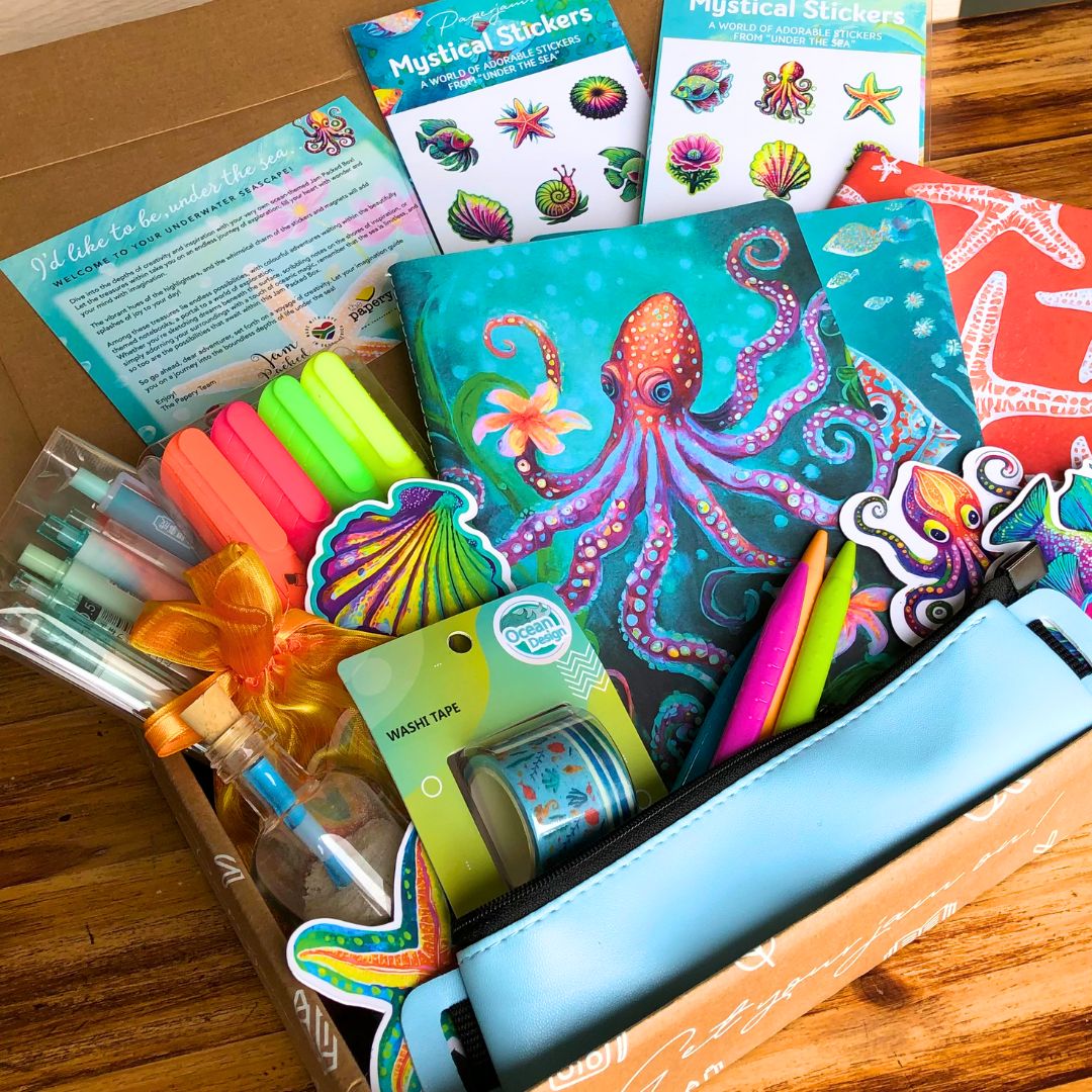 Ocean Treasures Gift box has colorful stationery set with a notebook, markers, and stickers in the box on a wooden surface