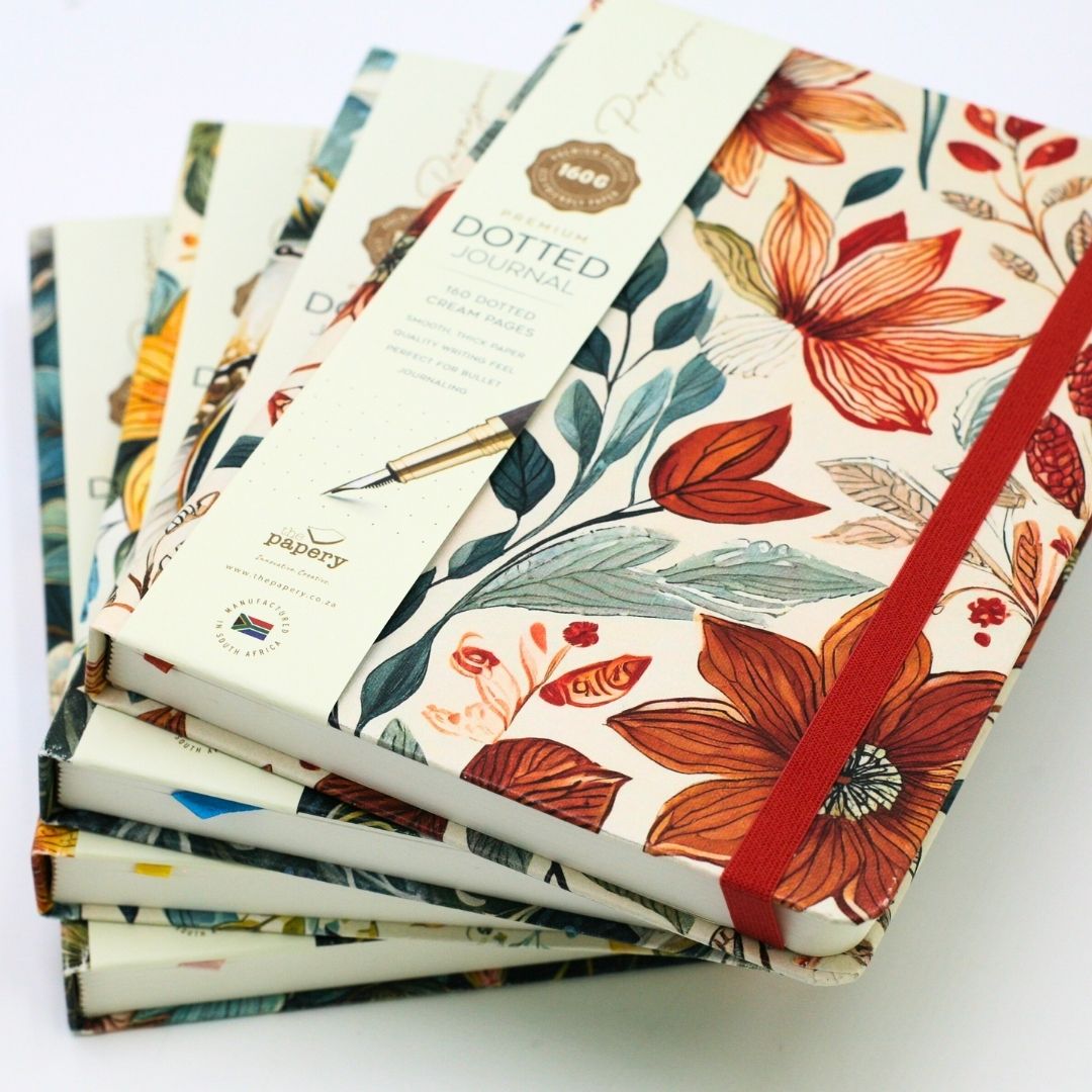 Stack of Premium hardcover A5 dotted Journals with matching ribbons for each design with stationery items on a white background