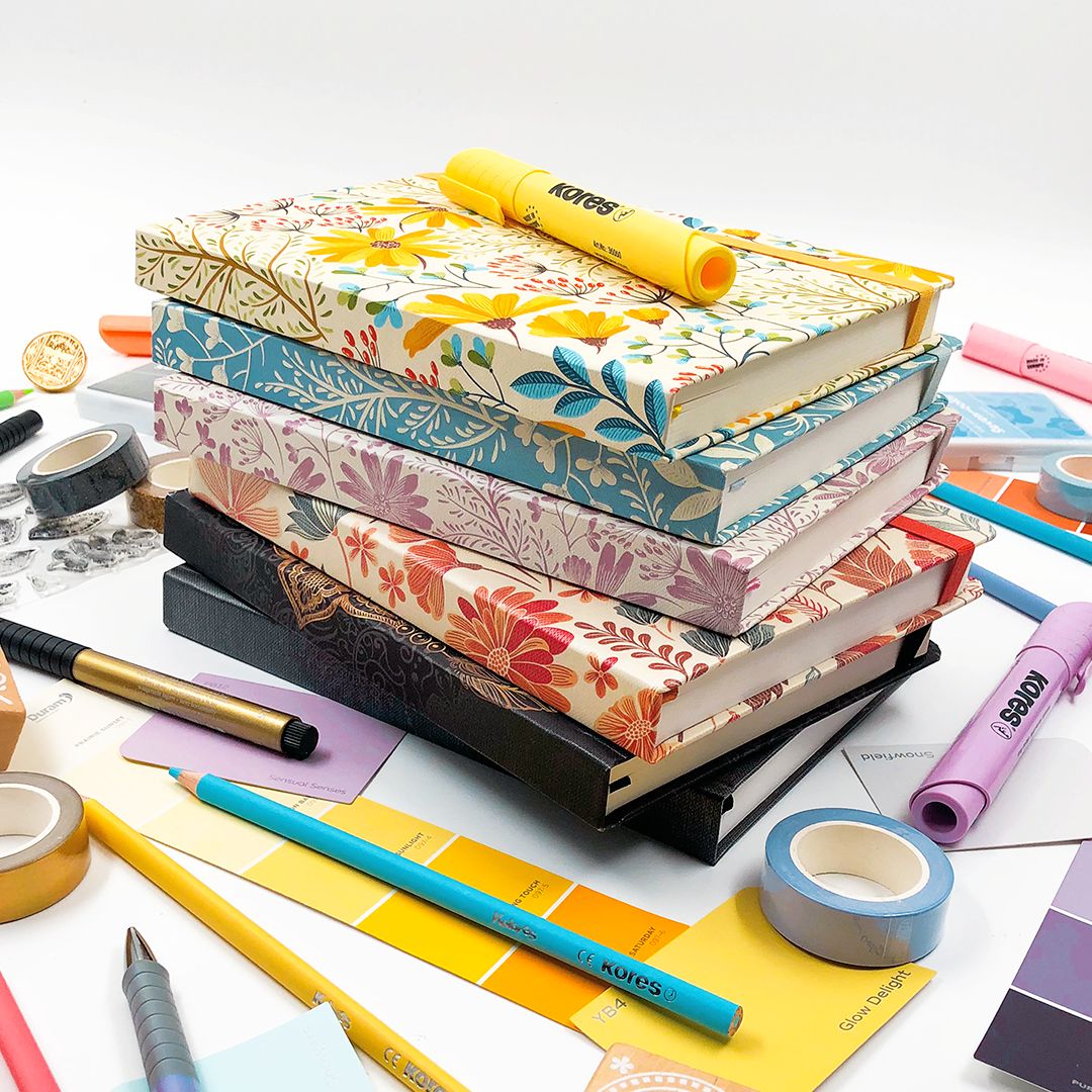 Stack of colorful hardcover notebooks with stationery items on a white background