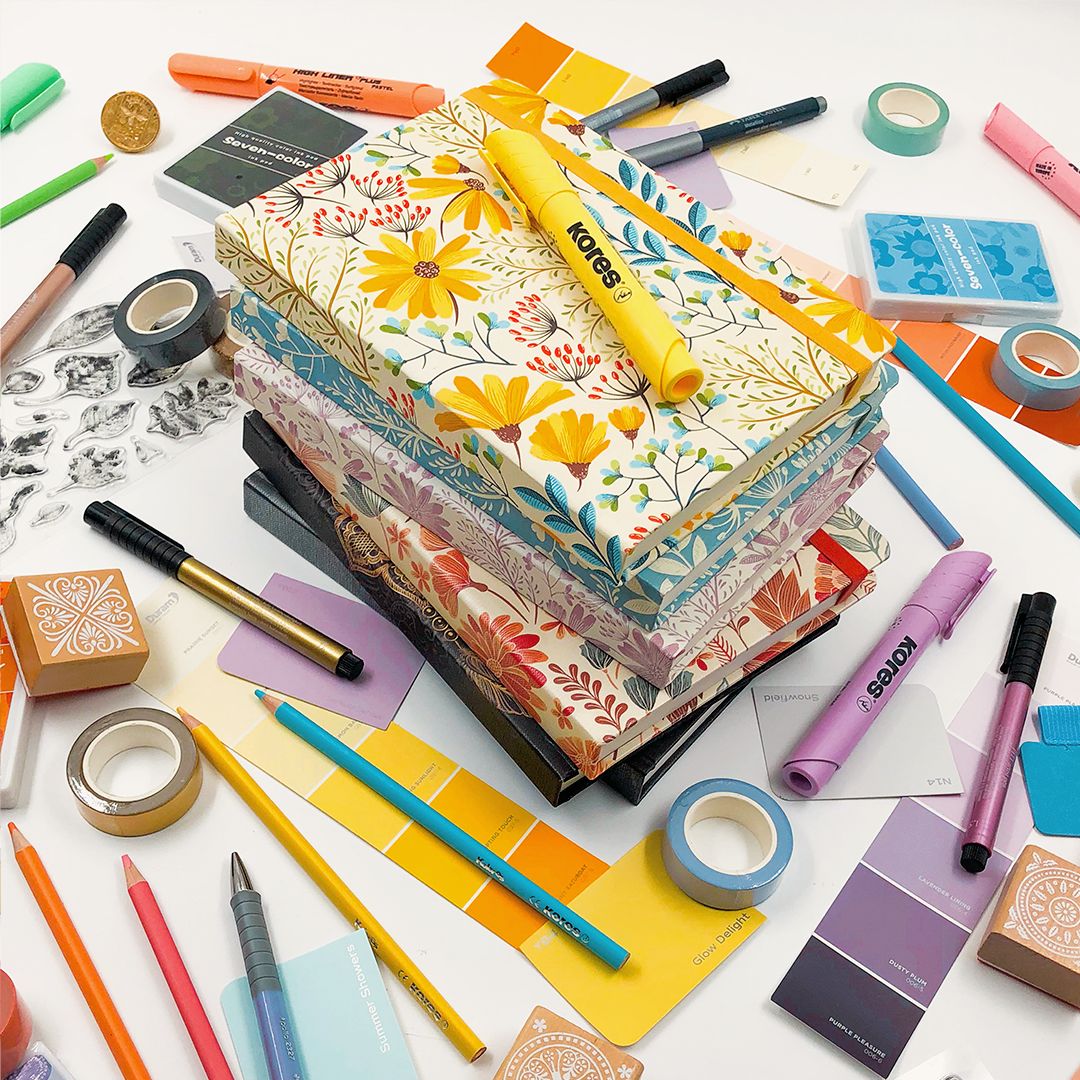 Colorful stationery items including markers, pens, and a floral hardcover notebooks on a white background