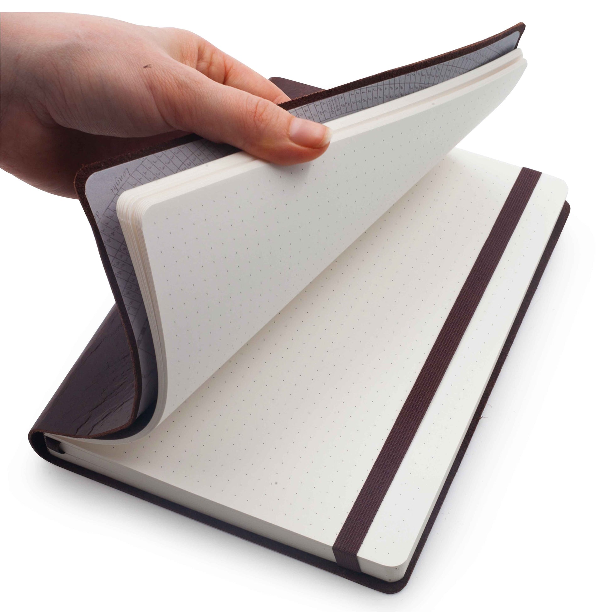 Inside dotted pages of an open brown genuine leather A6 notebook with a matching ribbon on a white background