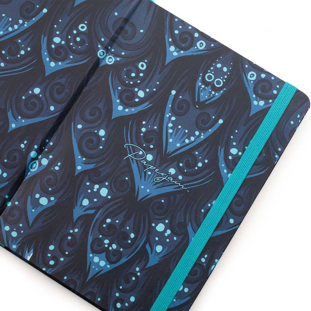 A close-up of a notebook cover featuring a dark navy and blue peacock feather pattern with light blue dots and swirls, accented by a bright turquoise elastic band.