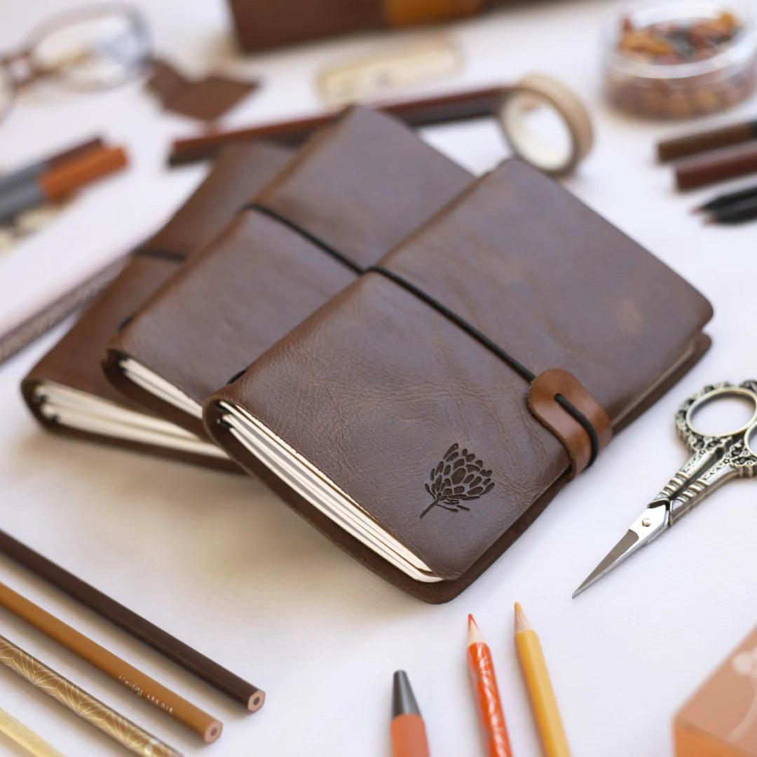 Brown leather notebook with a tree emblem on a white surface with stationery items.