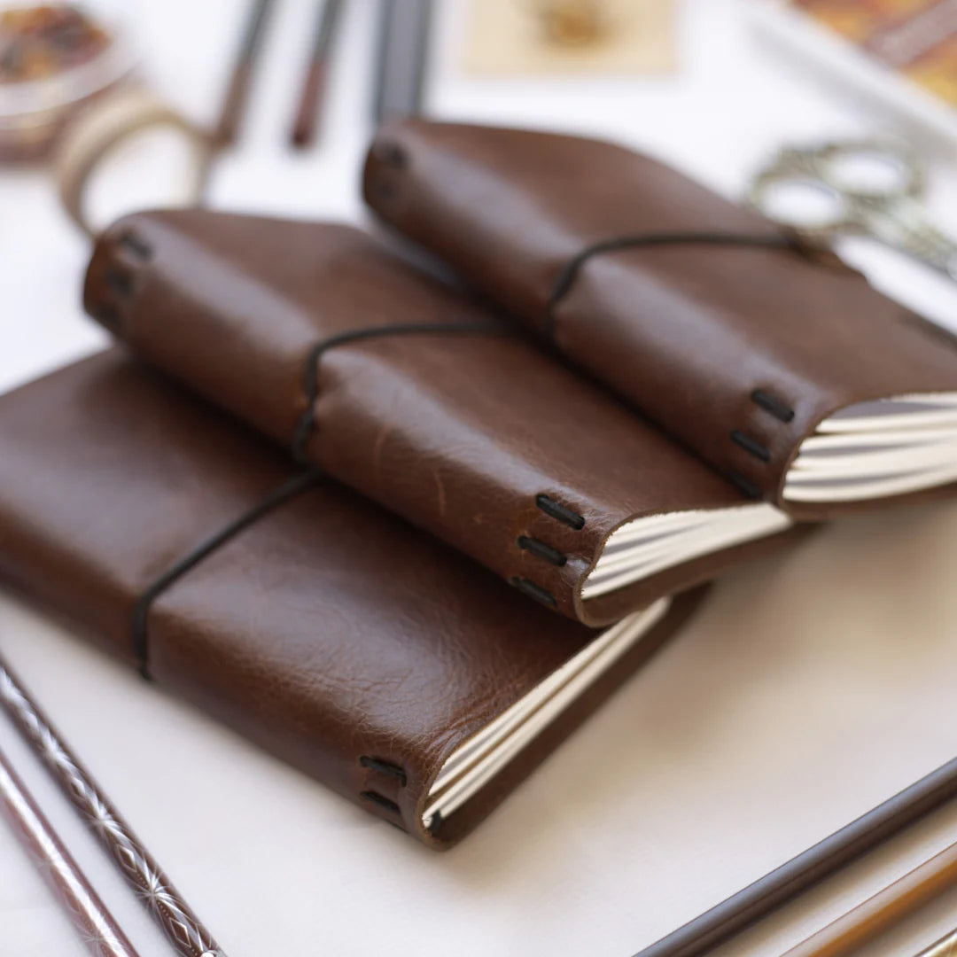 Three brown leather-bound notebooks stacked on a white surface