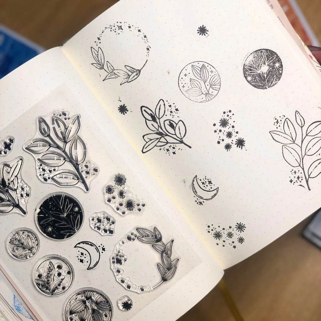 Sheet of black and white silicone stamps pressed in black ink pad and then into journal with nature-themed designs on a wooden surface.