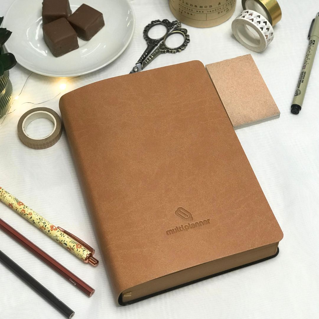 Flexi Multi-Planner in tan with surrounding stationary and chocolate on a white background