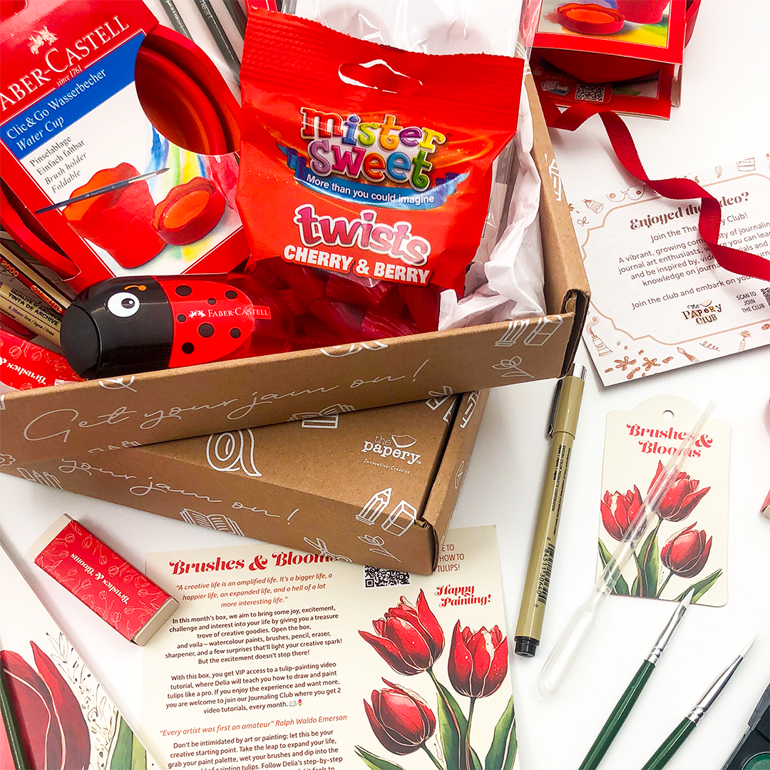 Open Brushes & Blooms gift Box that rocks containing stationery items with a focus on red packaging and art supplies.