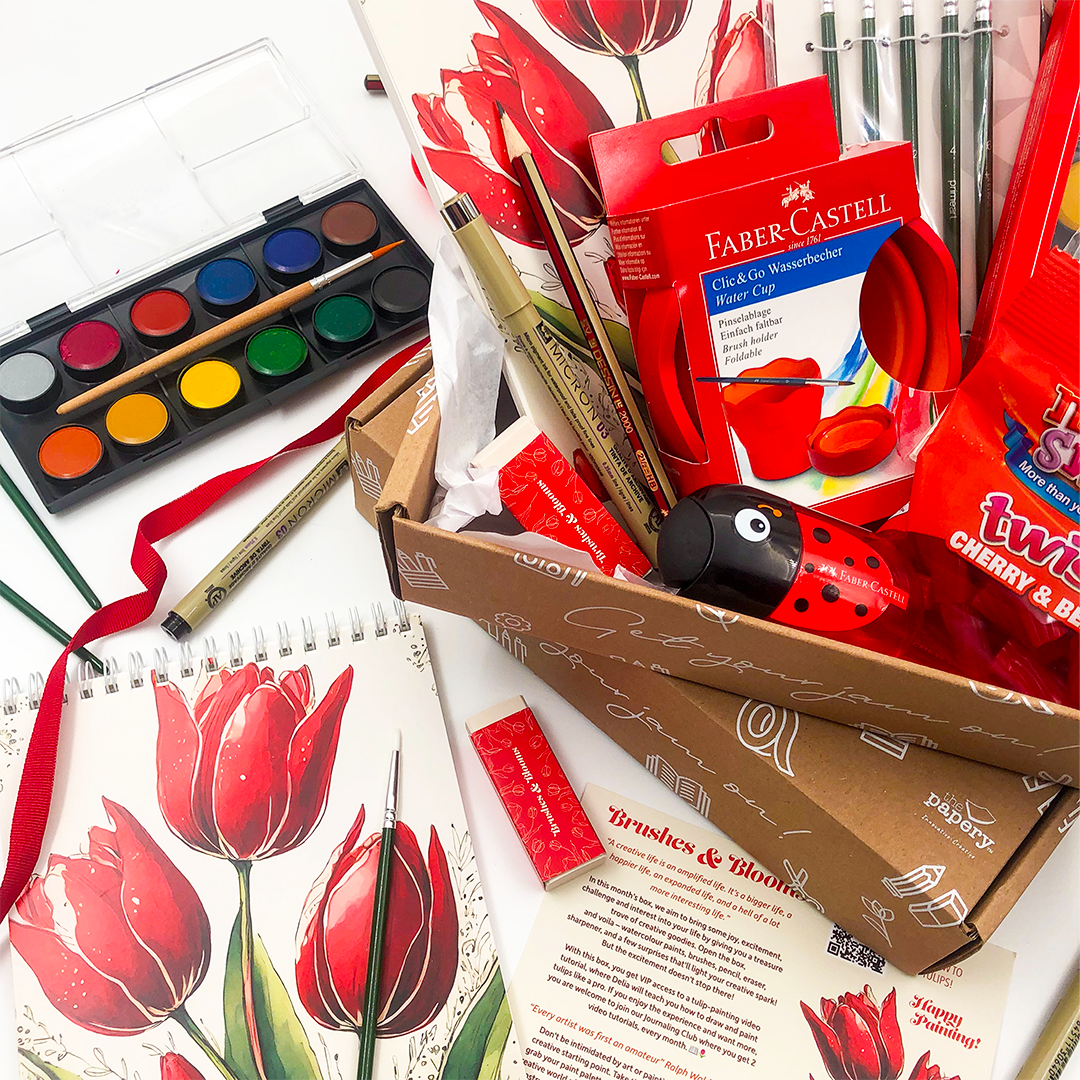 Brushes & Blooms gift Box that rocks has Art supplies including watercolors, brushes, and a box of Faber-Castell products on a white background.